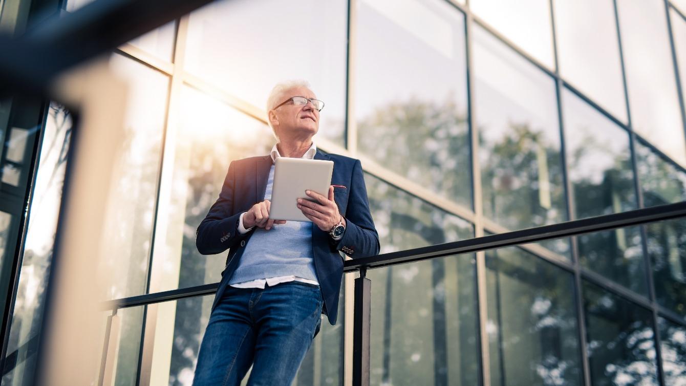 Older businessman stands outside an office building working on a tablet