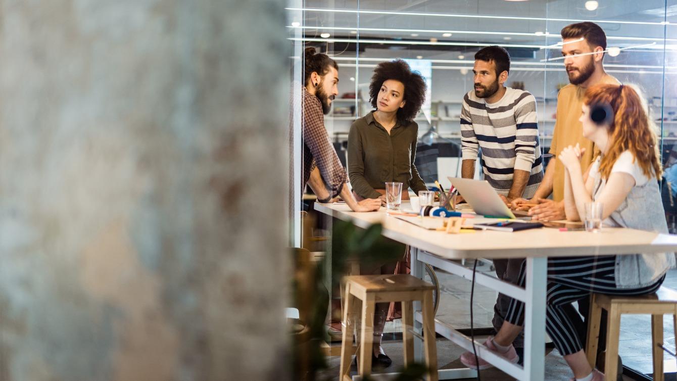 Group of people have a stand up conversation around a desk