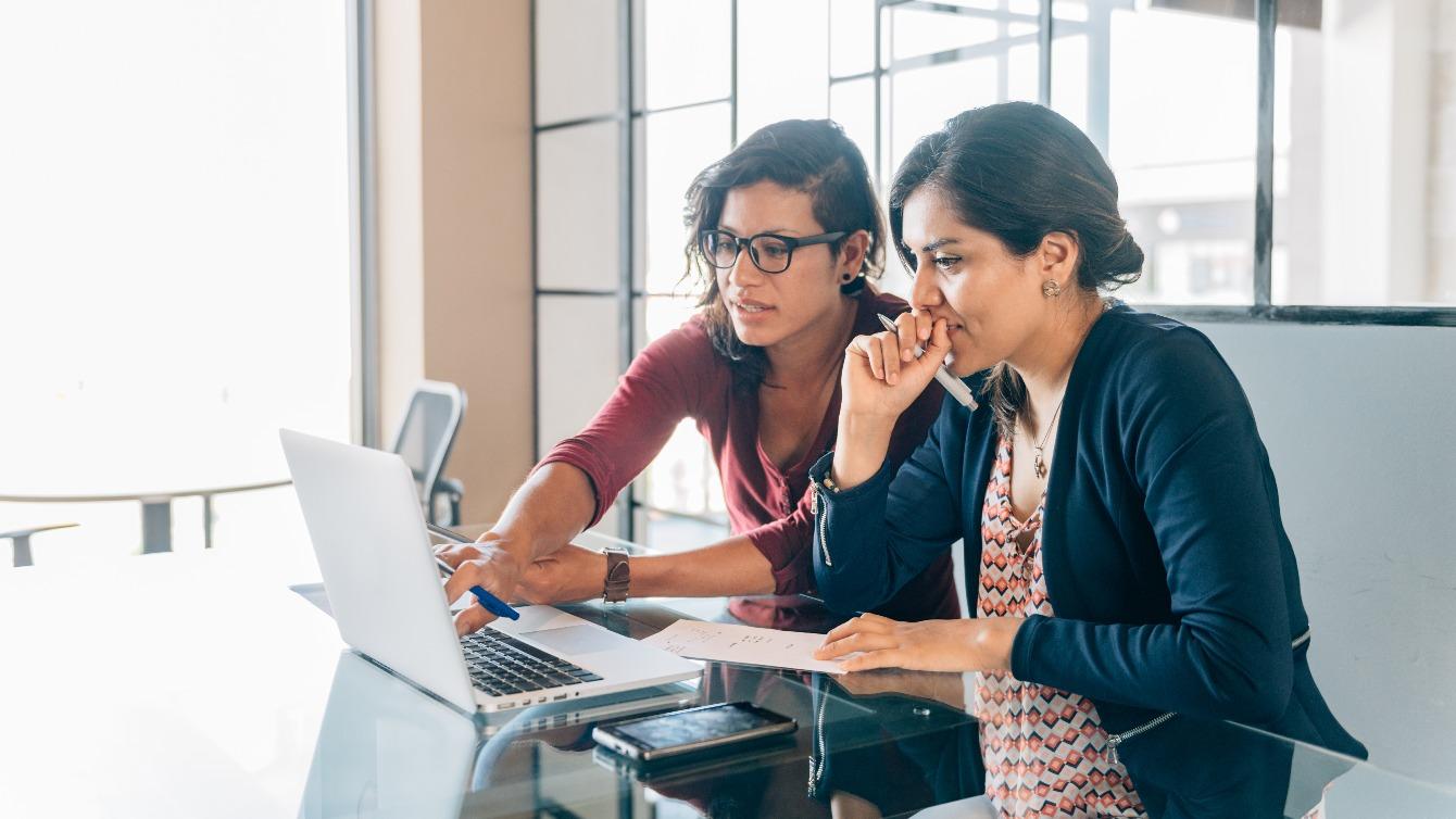 Two women in a meeting room discussing work on a laptop